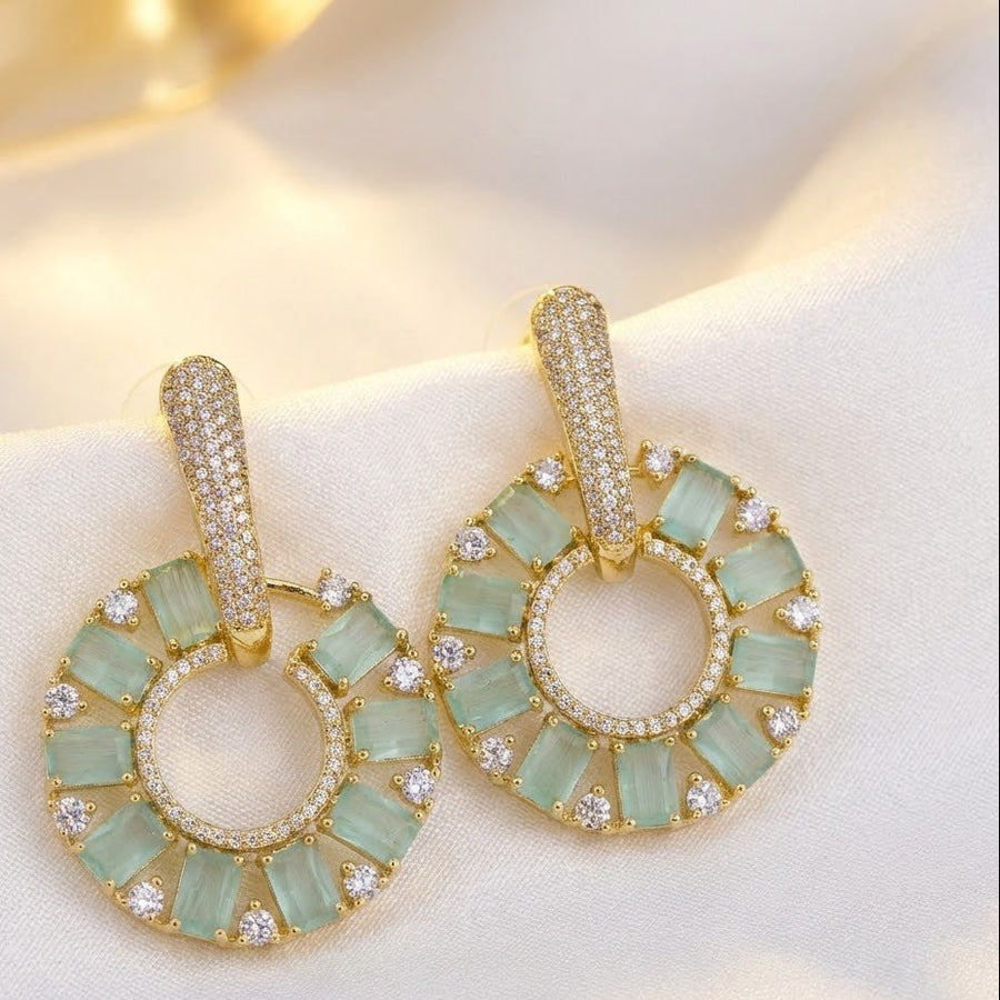 Light green stone circle drop earrings held delicately in hand with bright sunlight