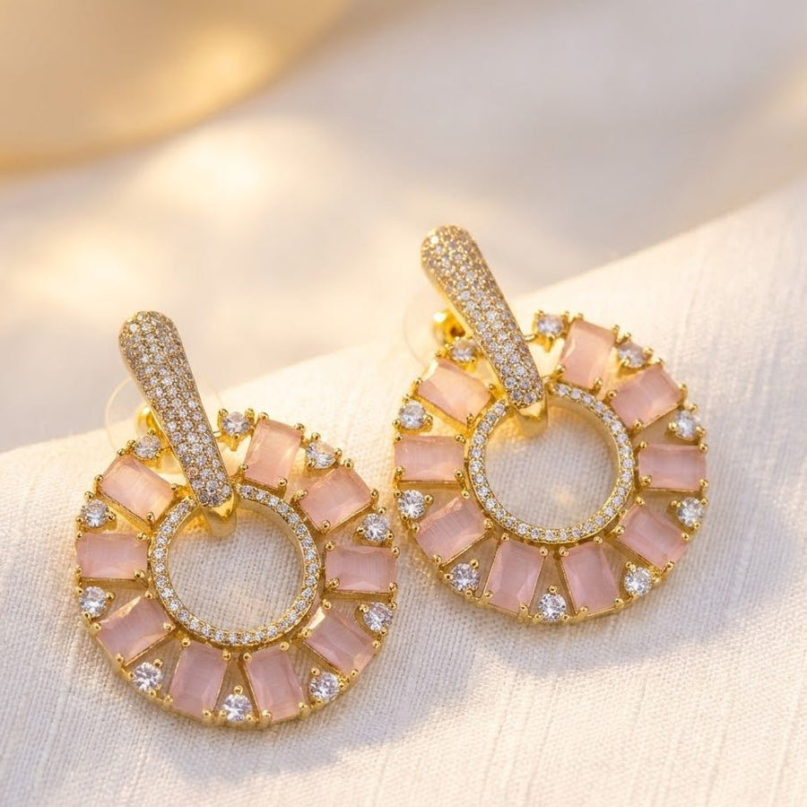 Close-up of gold plated pink stone circle drop earrings resting on beige fabric