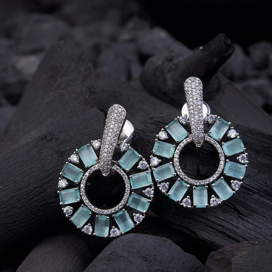 Silver plated clear stone circle drop earrings styled on soft white fabric reflecting light