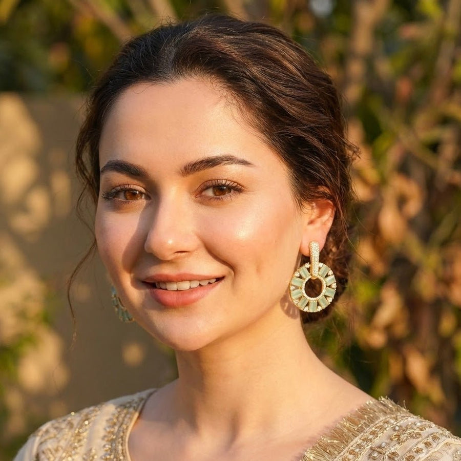Close-up of gold plated mint green stone circle drop earrings on black rough surface