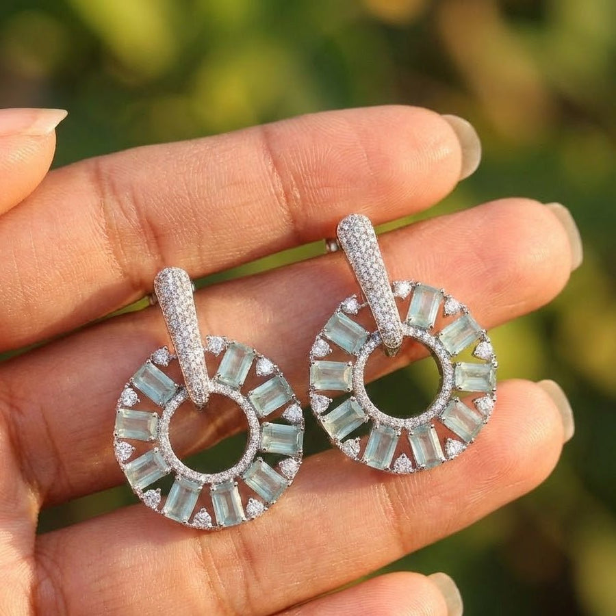 Gold plated mint green stone circle drop earrings held by hand outdoors in sunlight