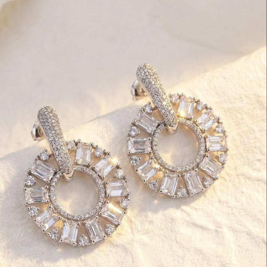 Silver plated clear stone circle drop earrings on soft white fabric reflecting light
