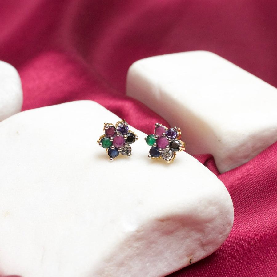 Floral gemstone stud earrings with multi-colored stones on white stone display with a magenta fabric background