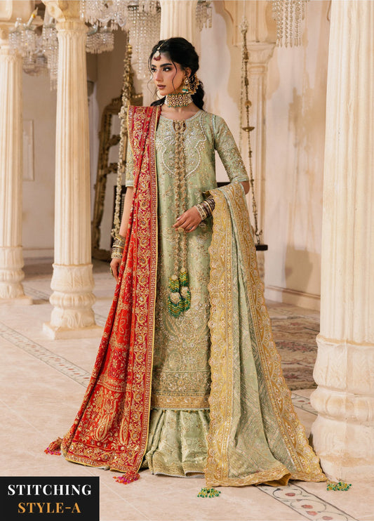 Woman in sage green embroidered formal suit with red and gold embroidered dupatta draped on one shoulder, indoors with elegant chandelier lighting.