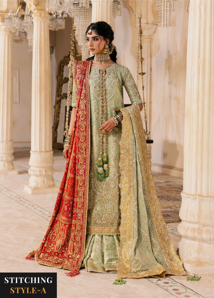 Woman in sage green embroidered formal suit with red and gold embroidered dupatta draped on one shoulder, indoors with elegant chandelier lighting.