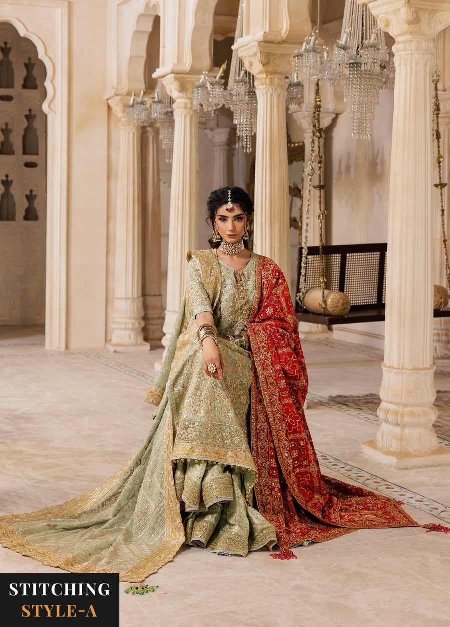 Seated woman wearing sage green embroidered formal suit with red dupatta, showcasing detailed embroidery and delicate tassels in a grand architectural setting.