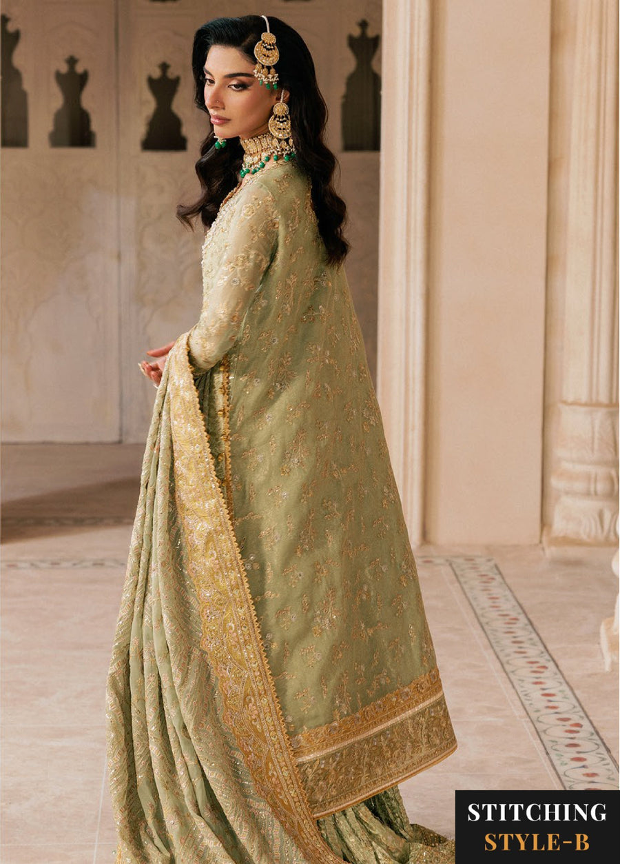 Back view of a woman in sage green embroidered formal suit with detailed gold zari embroidery on the dupatta and sharara, standing amid elegant cream pillars.