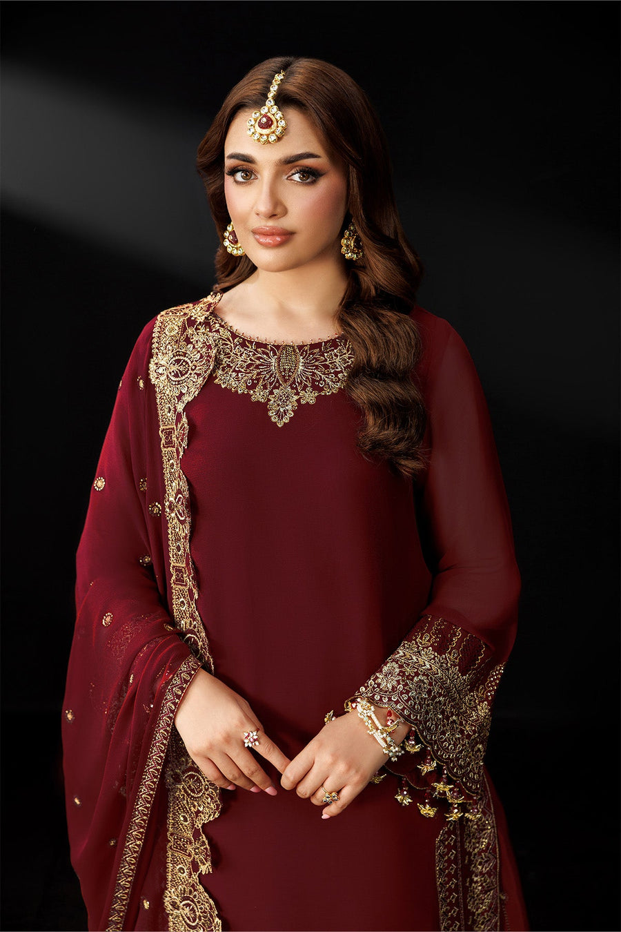 Upper body shot focusing on embroidered neckline and sleeves of maroon traditional suit
