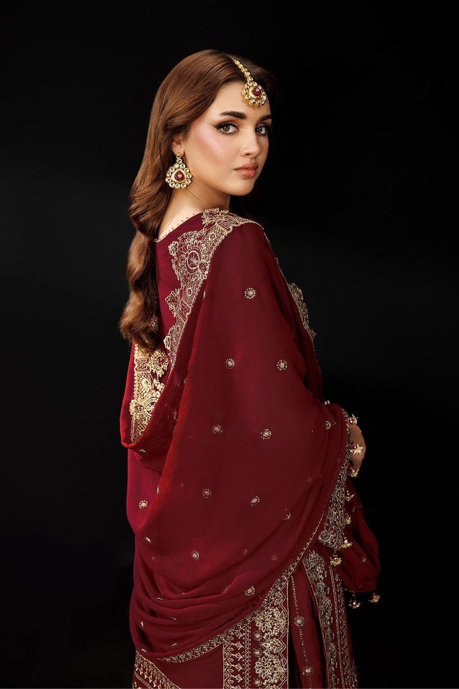 Woman standing with hands clasped wearing maroon suit and detailed gold embroidery