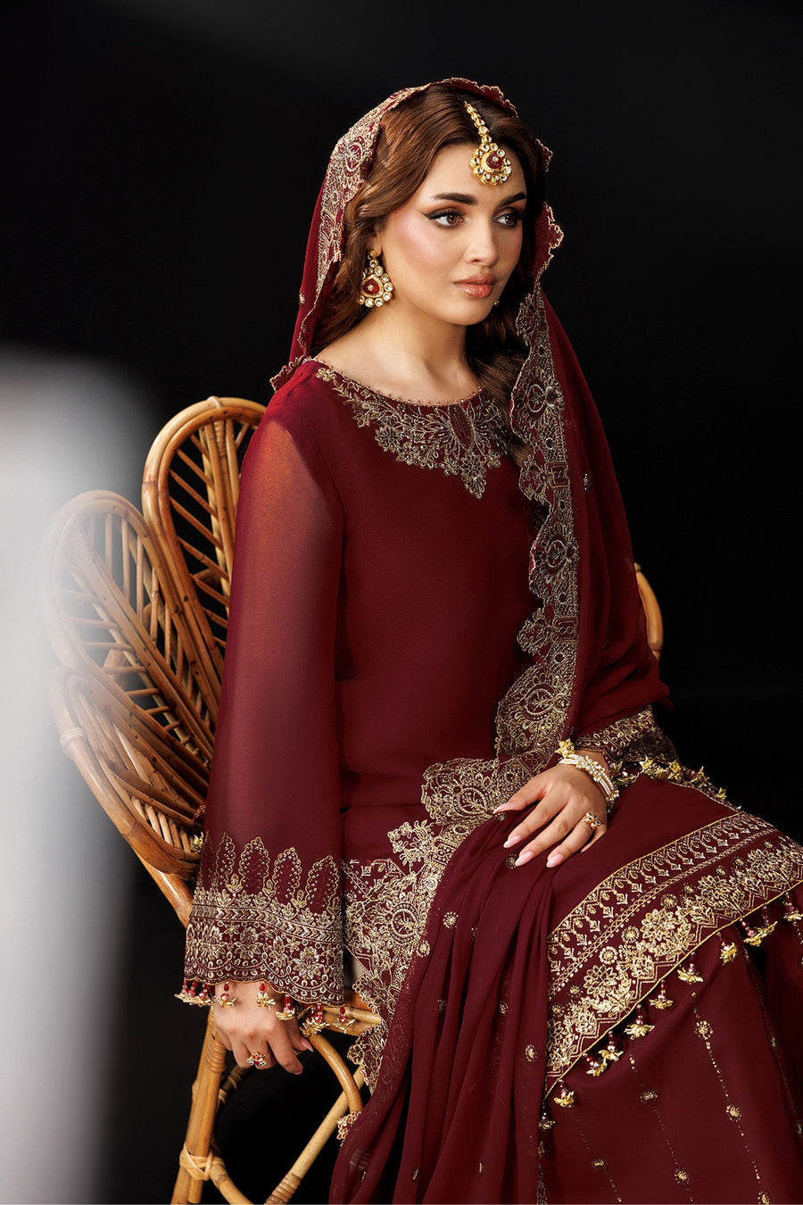 Seated woman in maroon suit with detailed embroidery and matching accessories