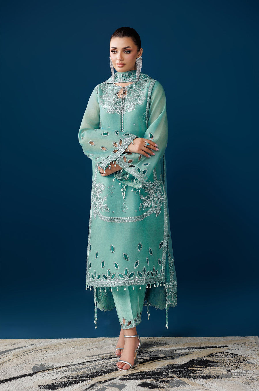 Full view of model in embroidered sea glass green suit with matching pants and dupatta, standing on patterned carpet