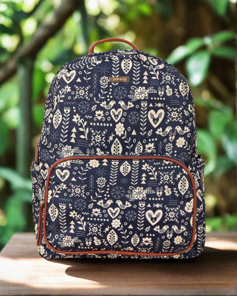 Navy blue backpack with cream floral and geometric tribal patterns on wooden surface with blurred greenery background