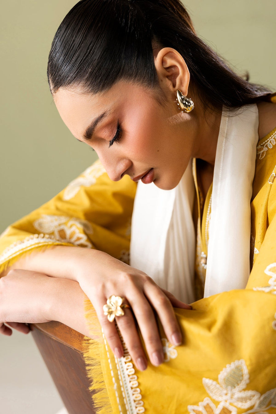 Full length side view of the model standing in embroidered mustard yellow shirt, white embroidered pants, and ombré dupatta with pearl-studded sandals