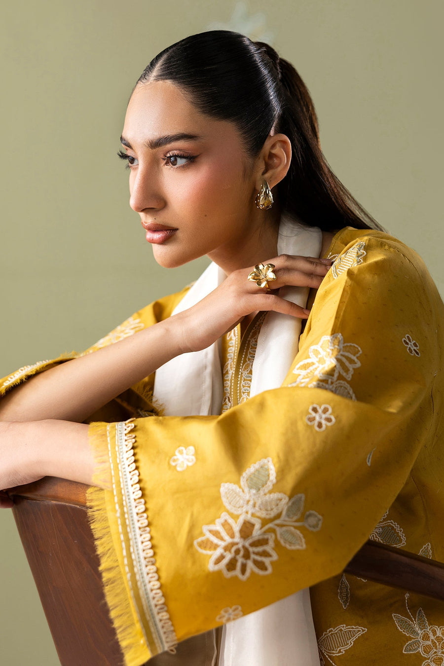 Model posing with arm resting on chair, highlighting sleeve embroidery and pearl-studded earrings and rings