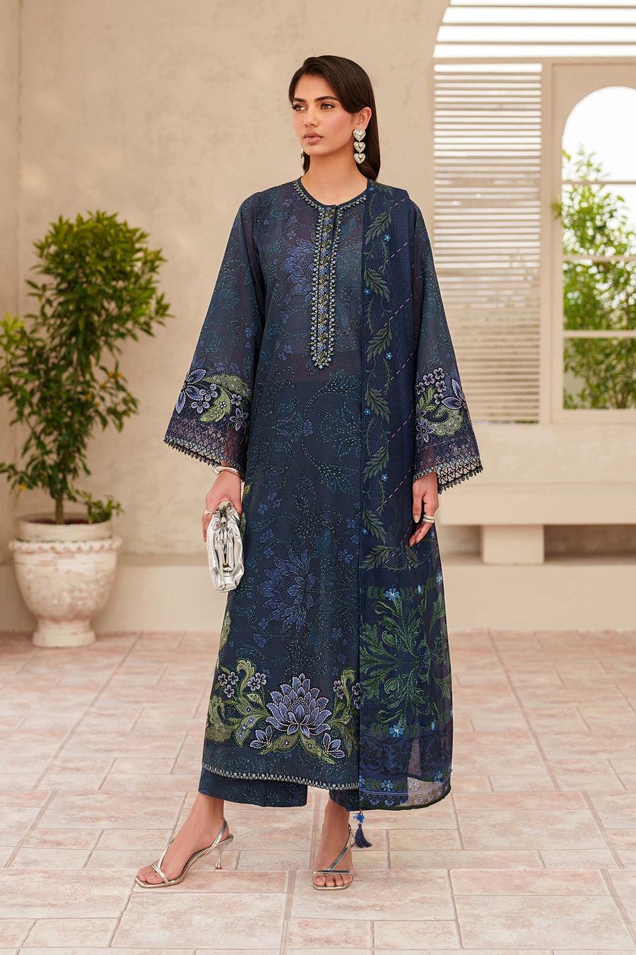 Woman wearing elegant navy three-piece embroidered lawn suit holding a silver clutch and wearing silver strappy heels