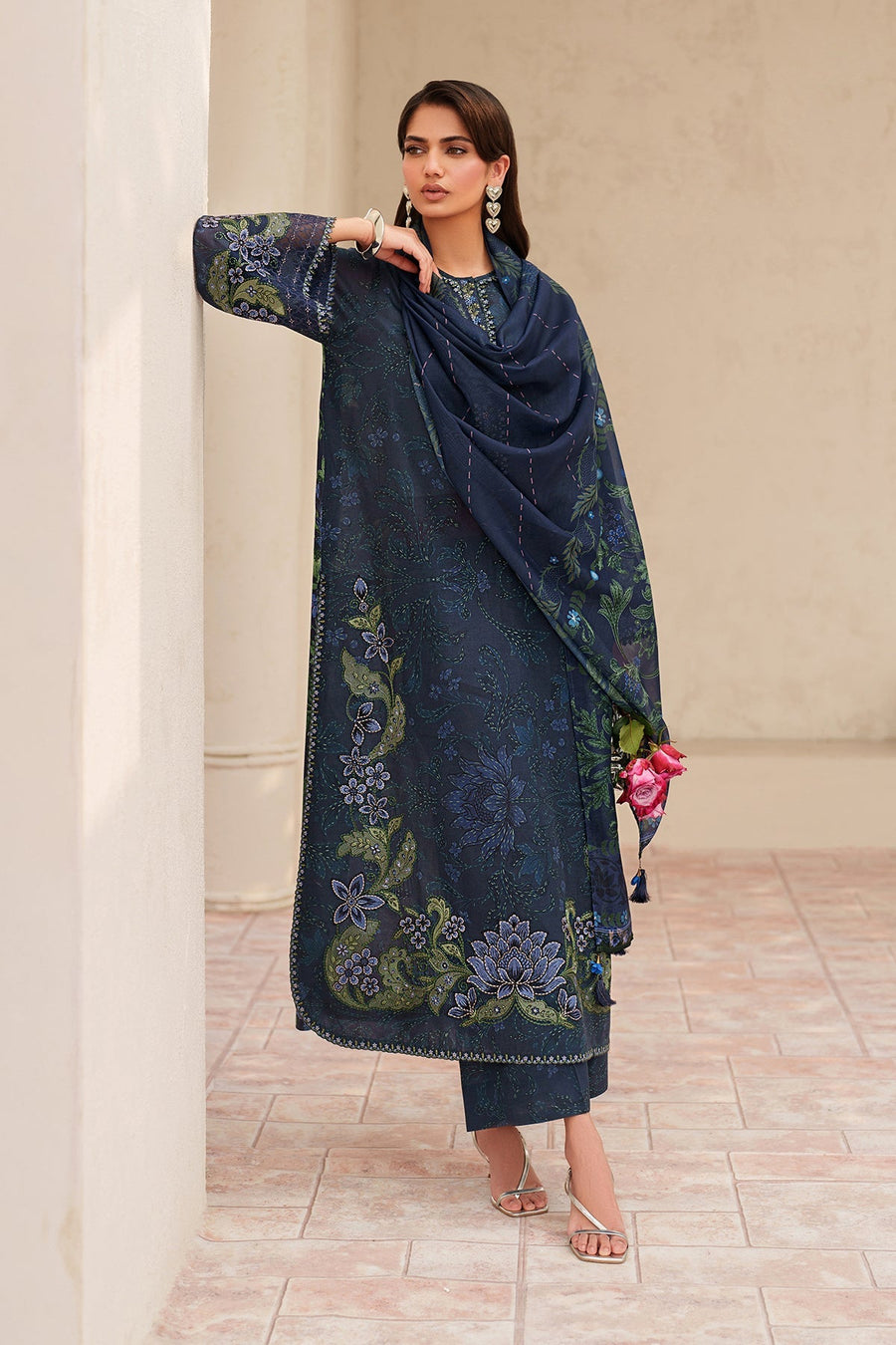 Full view of woman in navy embroidered lawn outfit styled with silver accessories and holding pink roses