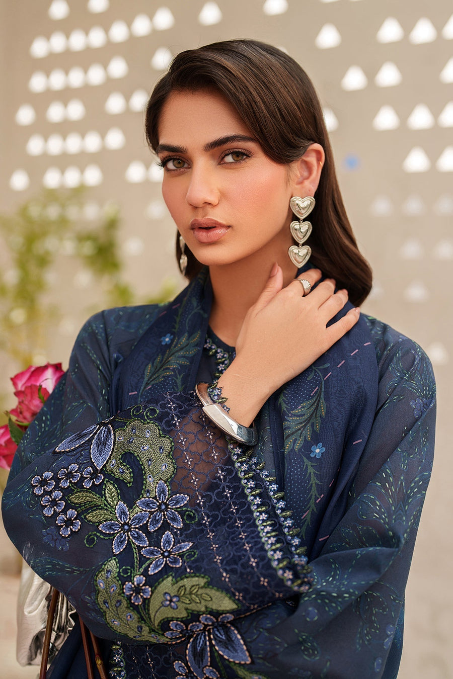 Close-up of sleeve embroidery and silver bracelet with woman holding pink roses
