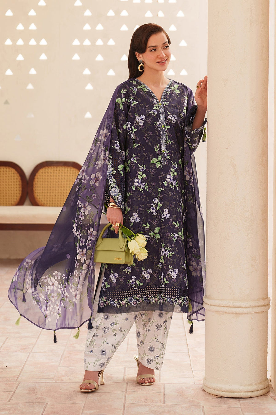 Close-up portrait of woman smiling, dressed in a navy floral embroidered lawn suit, holding a pale green handbag and white roses.
