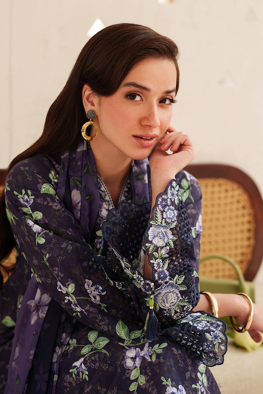 Close-up of a woman's arms showing intricate floral embroidery and scalloped lace cuffs on navy kurta sleeves, accessorized with gold bangles and rings.