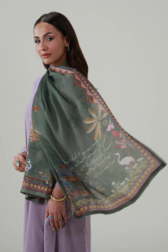 Woman wearing a deep green crinkle silk scarf with artistic calligraphy and floral bird motifs draped elegantly over her shoulders.