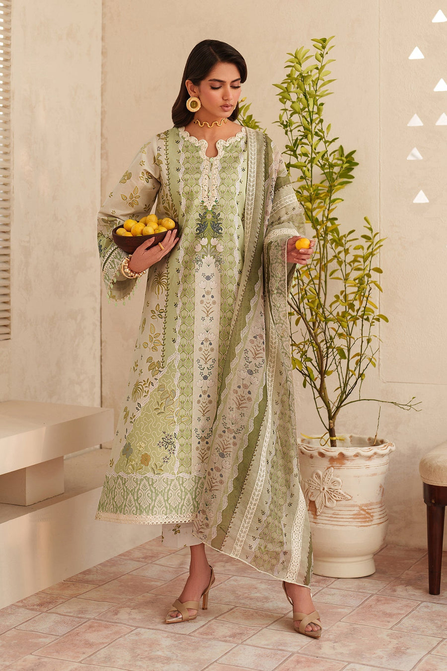 Full front view of woman in embroidered lawn suit with patterned trousers and detailed dupatta, styled with beige sandals and statement jewelry