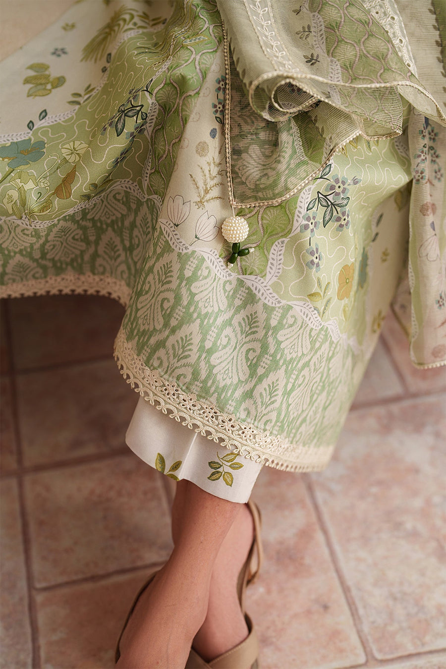 Close-up of hem showing lace embroidery on green printed fabric and floral patterned trousers beneath
