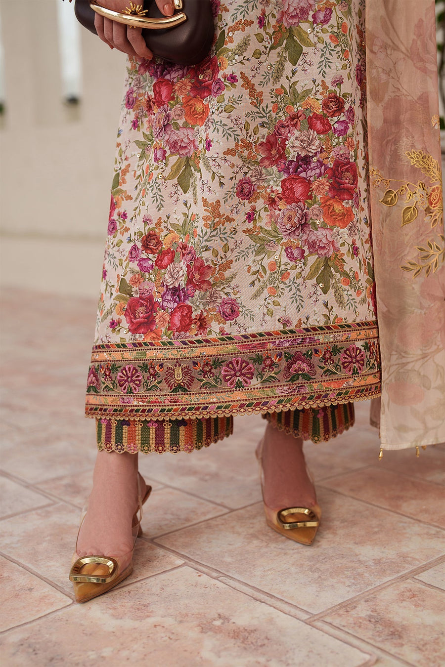 Close-up on embroidered sleeve cuff, floral print fabric, and model holding a brown clutch with golden handle