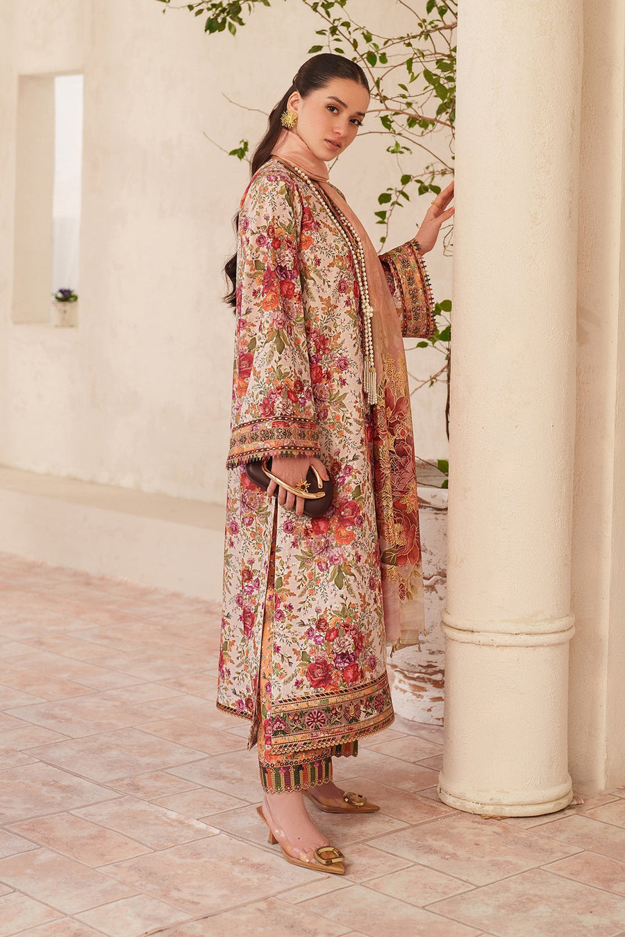Side view of the model standing wearing the embroidered lawn suit with peach dupatta and golden shoes