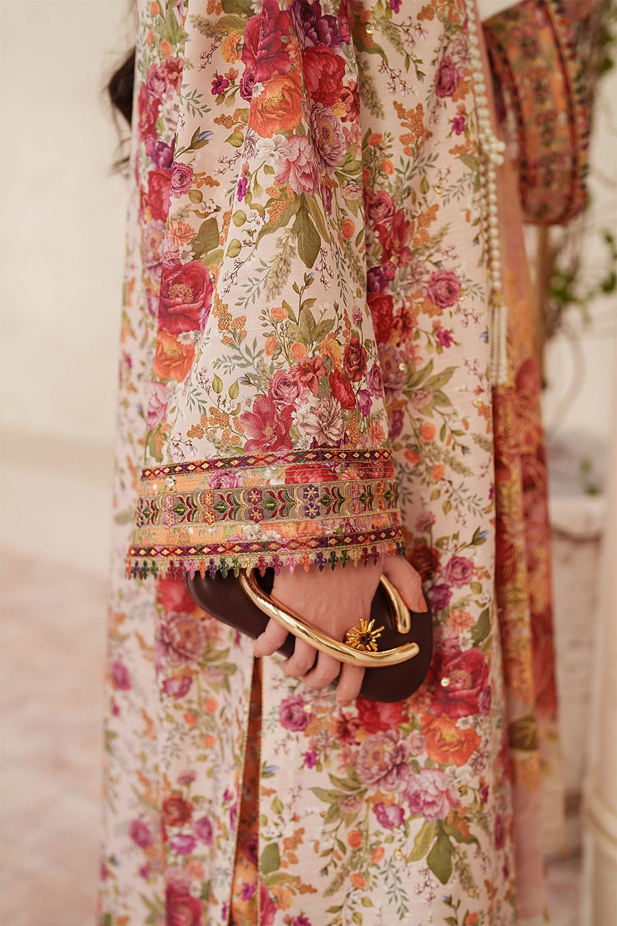 Model leaning on wall showing detailed embroidery on sleeves and dupatta with soft floral patterns