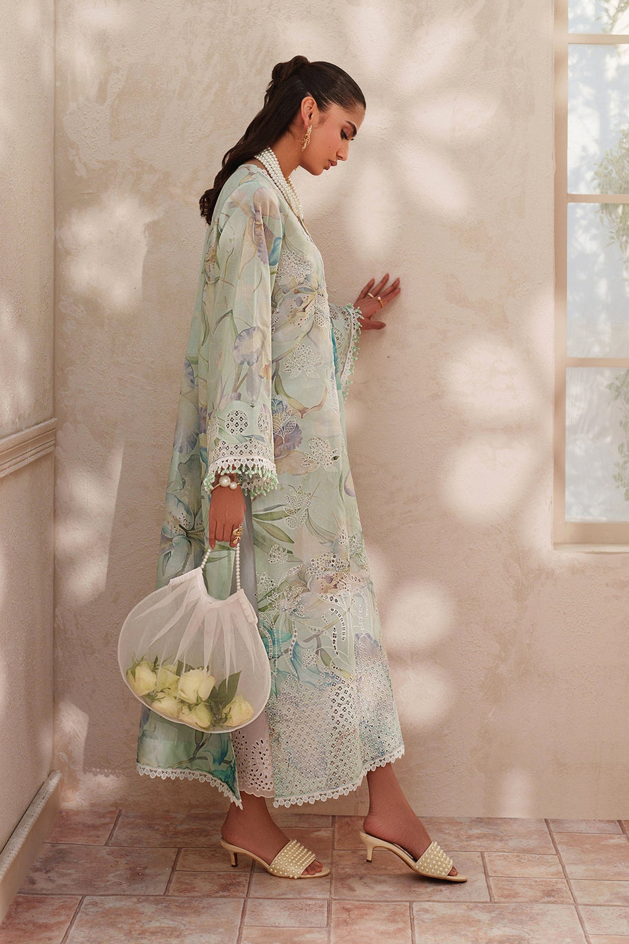 Model seated wearing elegant embroidered lawn suit showing detailed embroidery and lace with matching pastel dupatta draped over shoulder