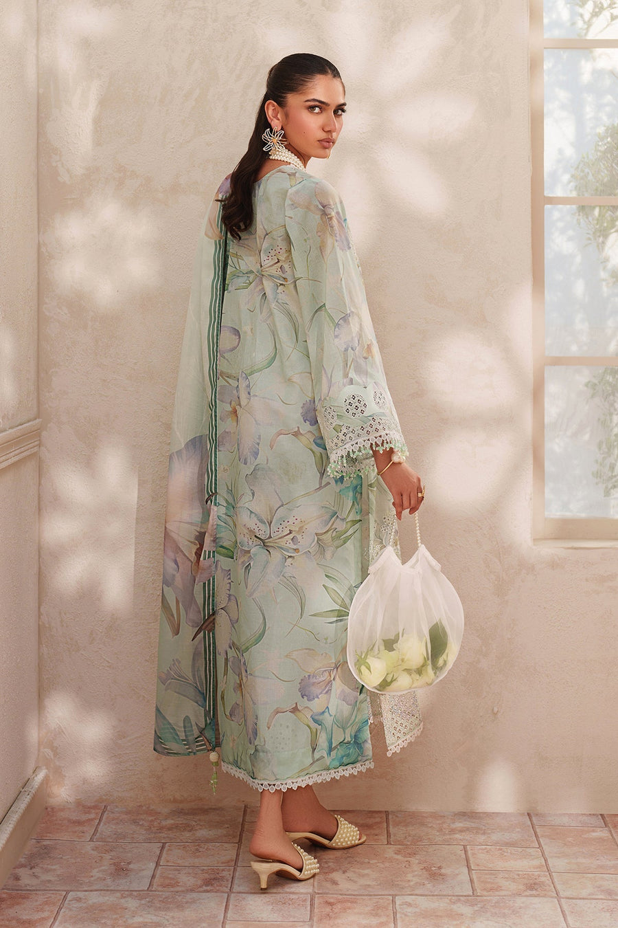 Back side view of woman in delicate floral embroidered lawn suit featuring long sleeves and flowing dupatta with digital floral print and bead tassels