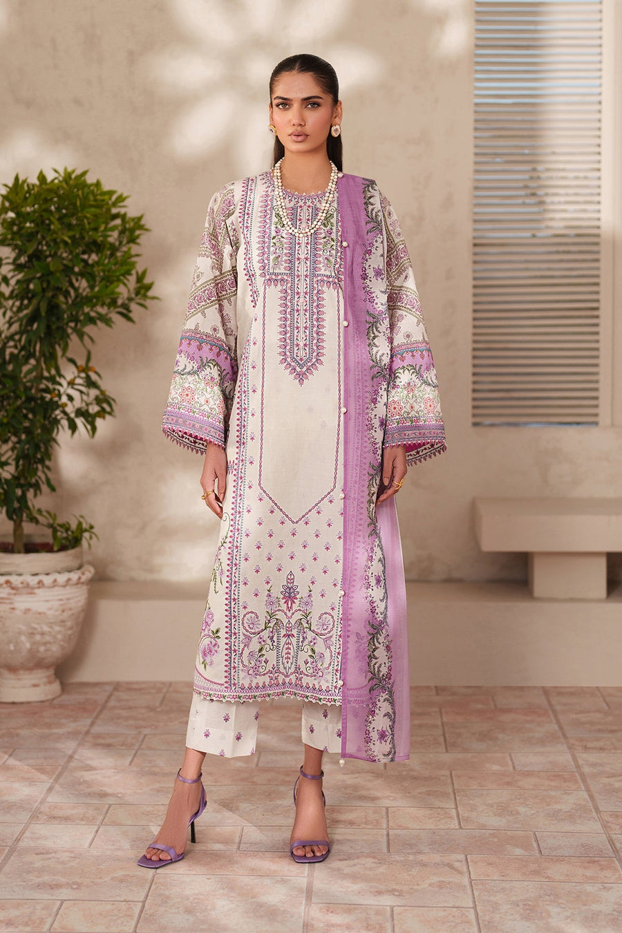 Front view of woman wearing embroidered floral lawn suit with lavender and pink patterns, paired with matching trousers and purple heeled sandals.