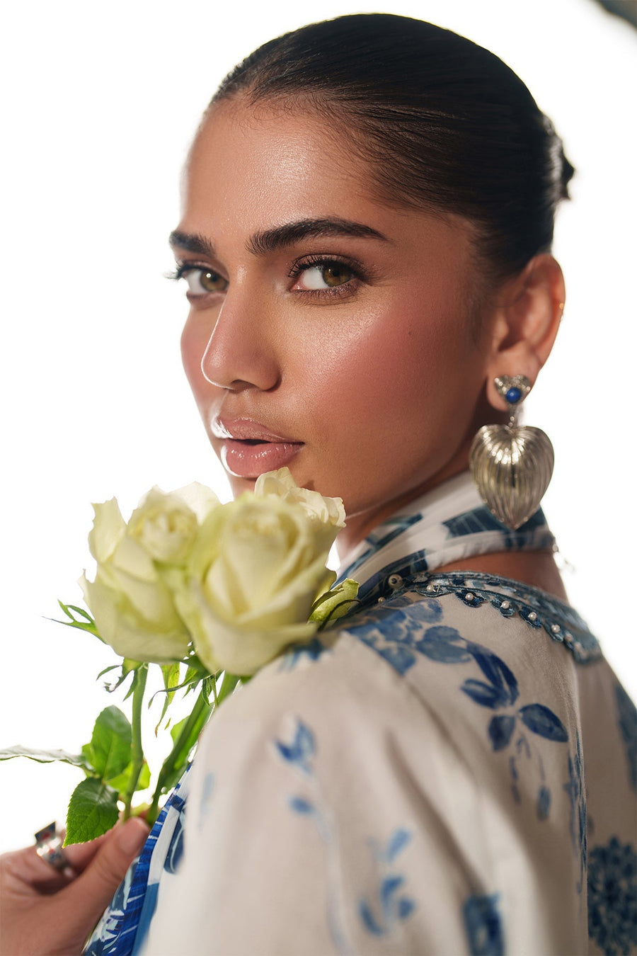 Artistic portrait of model holding white roses, featuring soft embroidery details and floral print from the outfit