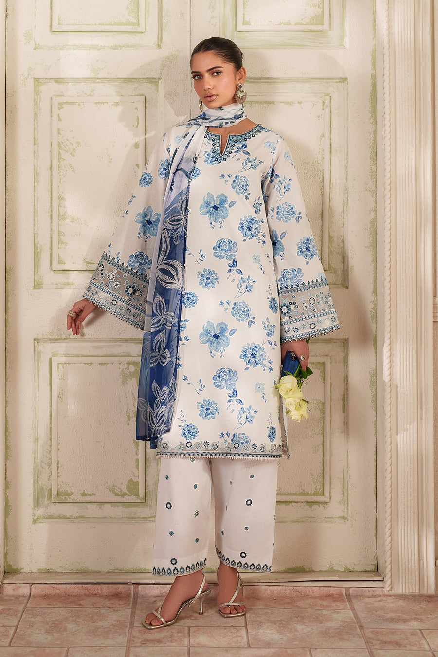 Front view of woman wearing white and blue floral embroidered three-piece outfit with tunic, cropped pants, and sheer blue floral dupatta