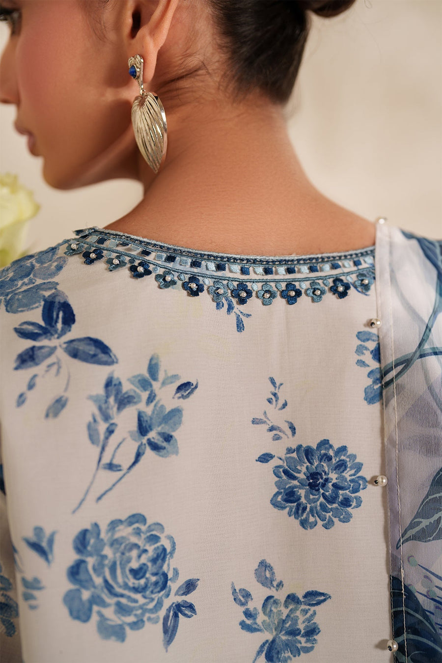 Full front view of woman standing indoors wearing white and blue embroidered lawn suit paired with silver strappy heels.