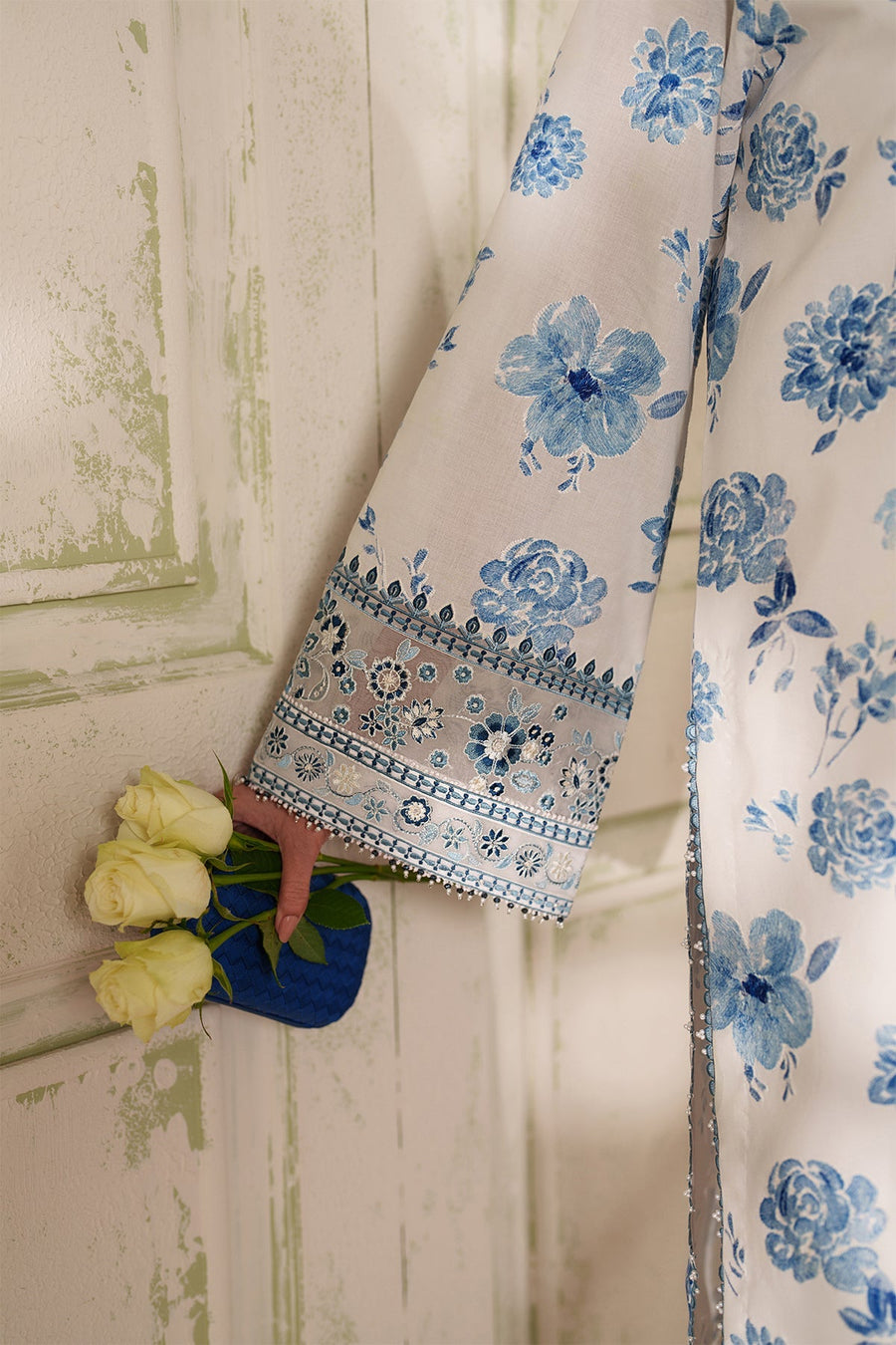 Close-up frontal view of neckline embroidery in blue thread and beads on white fabric along with floral print dupatta