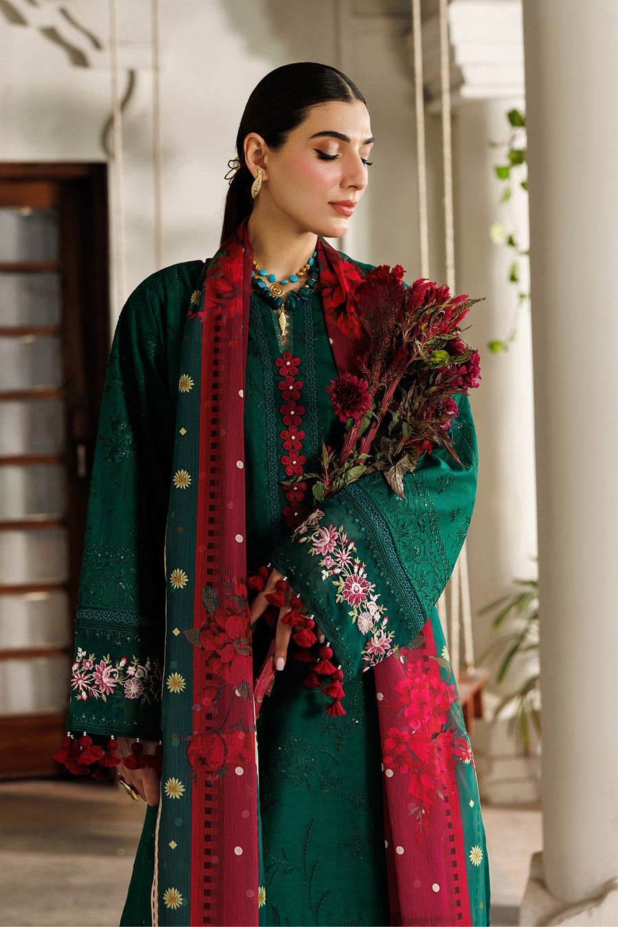Close-up of sleeve embroidery and tassel detail on emerald green lawn fabric with red floral dupatta