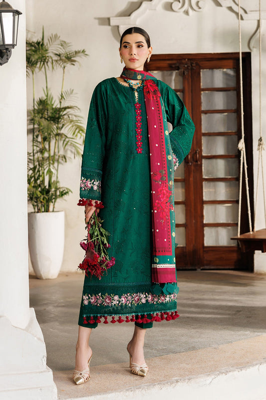 Woman wearing emerald green embroidered lawn suit with floral accents and red tassels, standing indoors holding red flowers