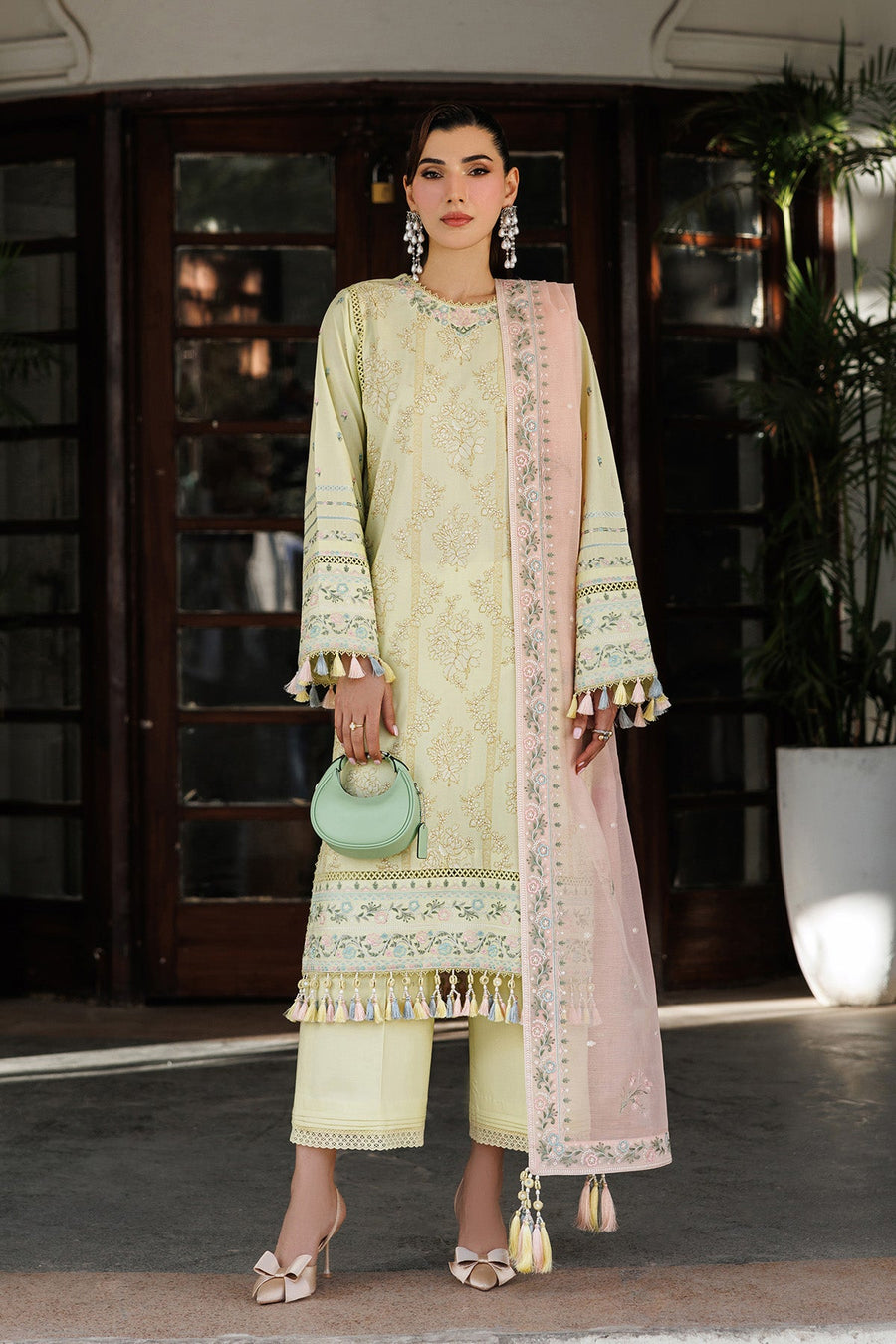 Woman wearing pastel yellow embroidered lawn shirt with tassel details and pastel pink floral embroidered dupatta holding a mint green handbag