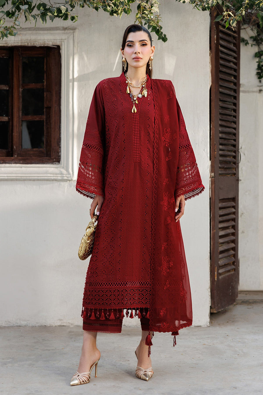 Front view of woman wearing red embroidered formal lawn suit with tinted gold accessories