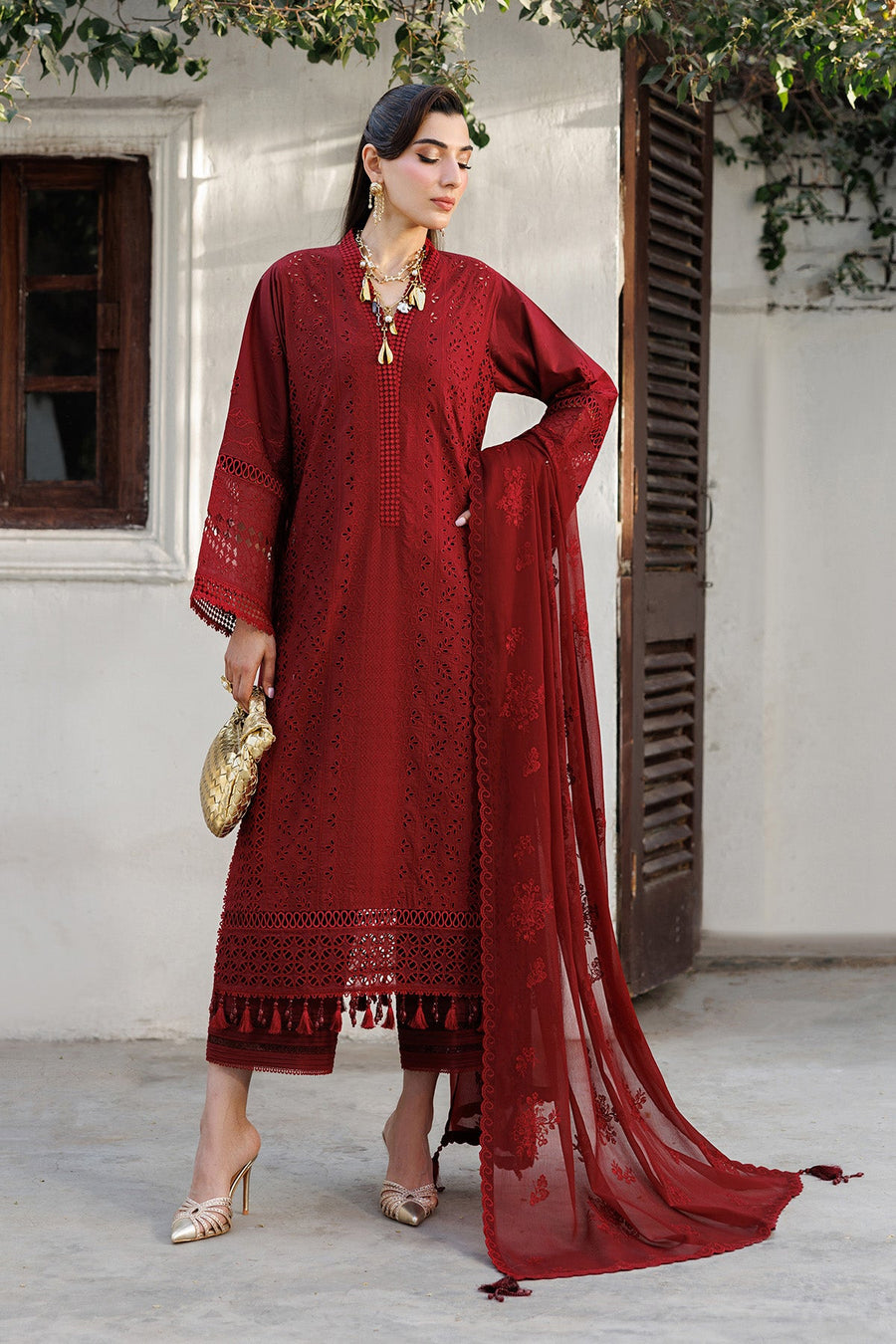 Model holding golden clutch showcasing embroidered sleeve and tassel details on red lawn suit