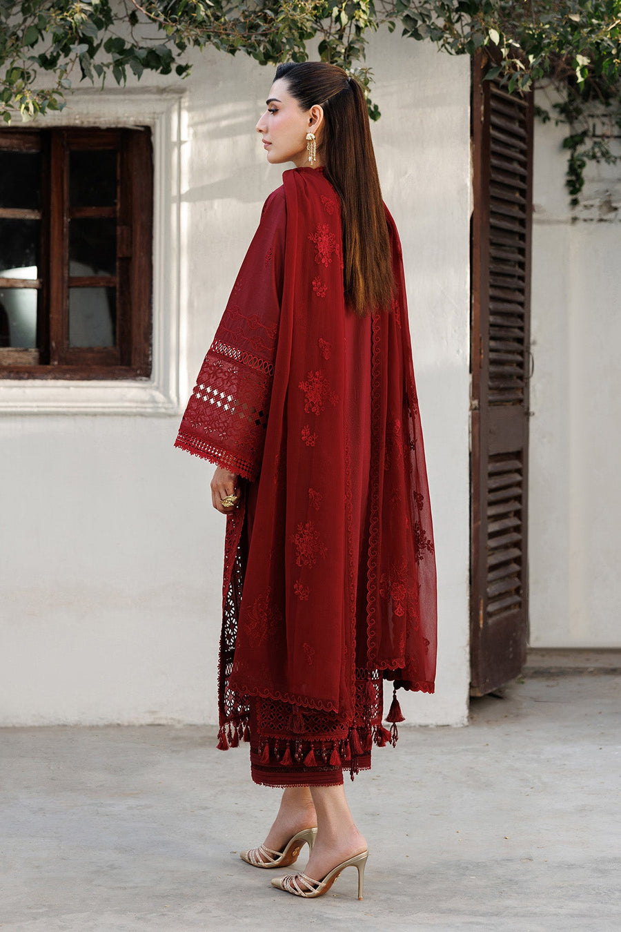 Side profile view of woman modeling red embroidered lawn suit with organza borders and tasselled dupatta