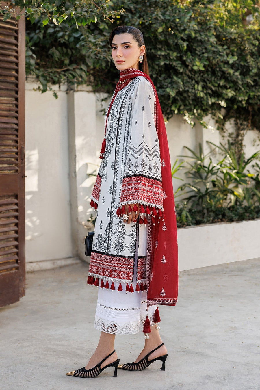 Side profile of woman in embroidered lawn suit showcasing tassels on sleeve and red embroidered dupatta