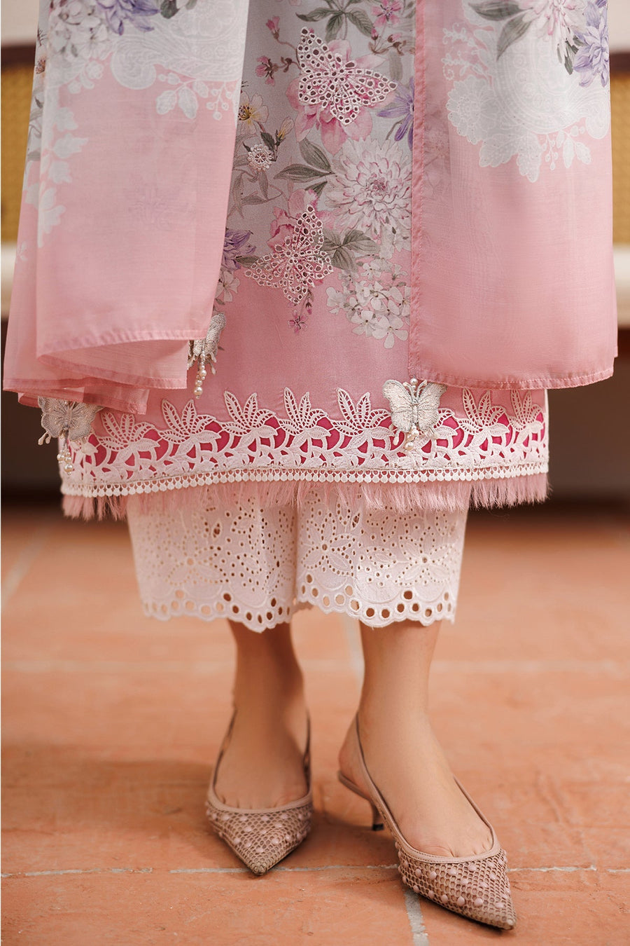 Front view portrait of woman in pastel floral embroidered lawn suit with organza neckline and layered pearl necklace holding a blush pink purse