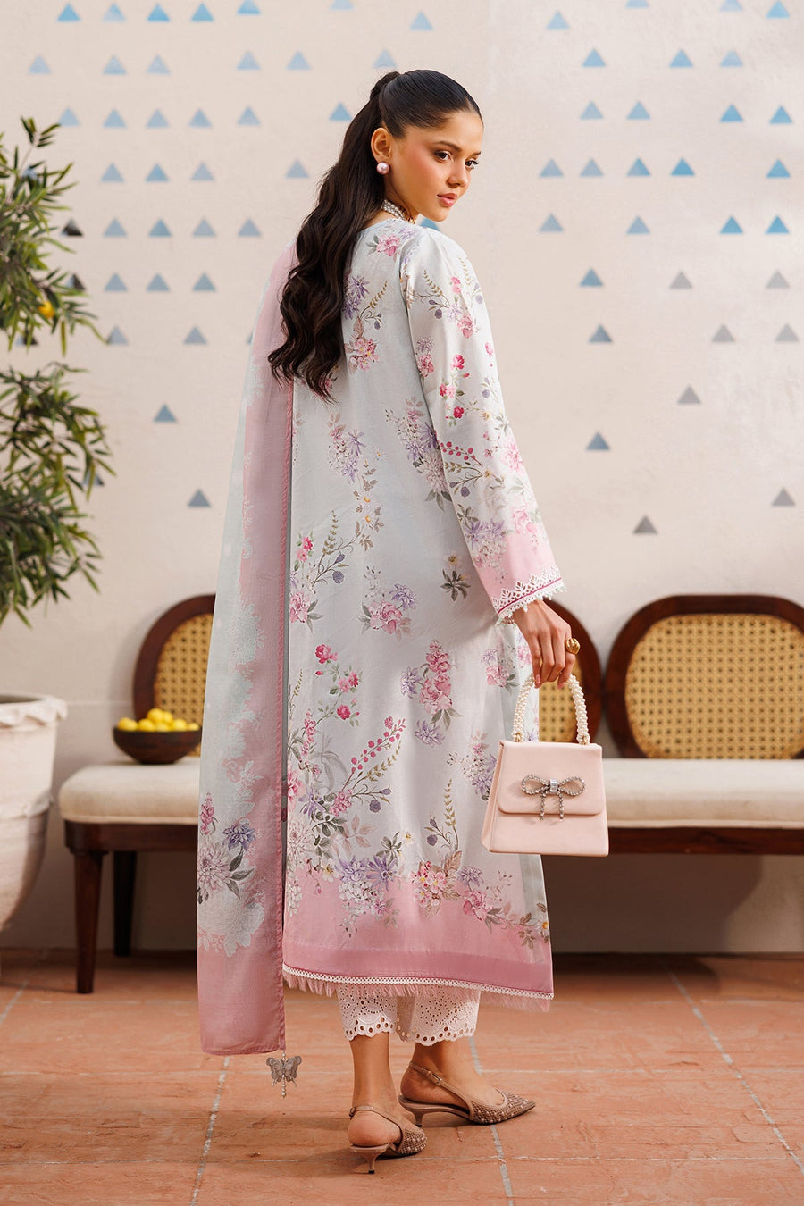 Back view of woman in floral embroidered lawn suit showcasing detailed floral pattern on sleeves and back along with pastel dupatta and small handbag