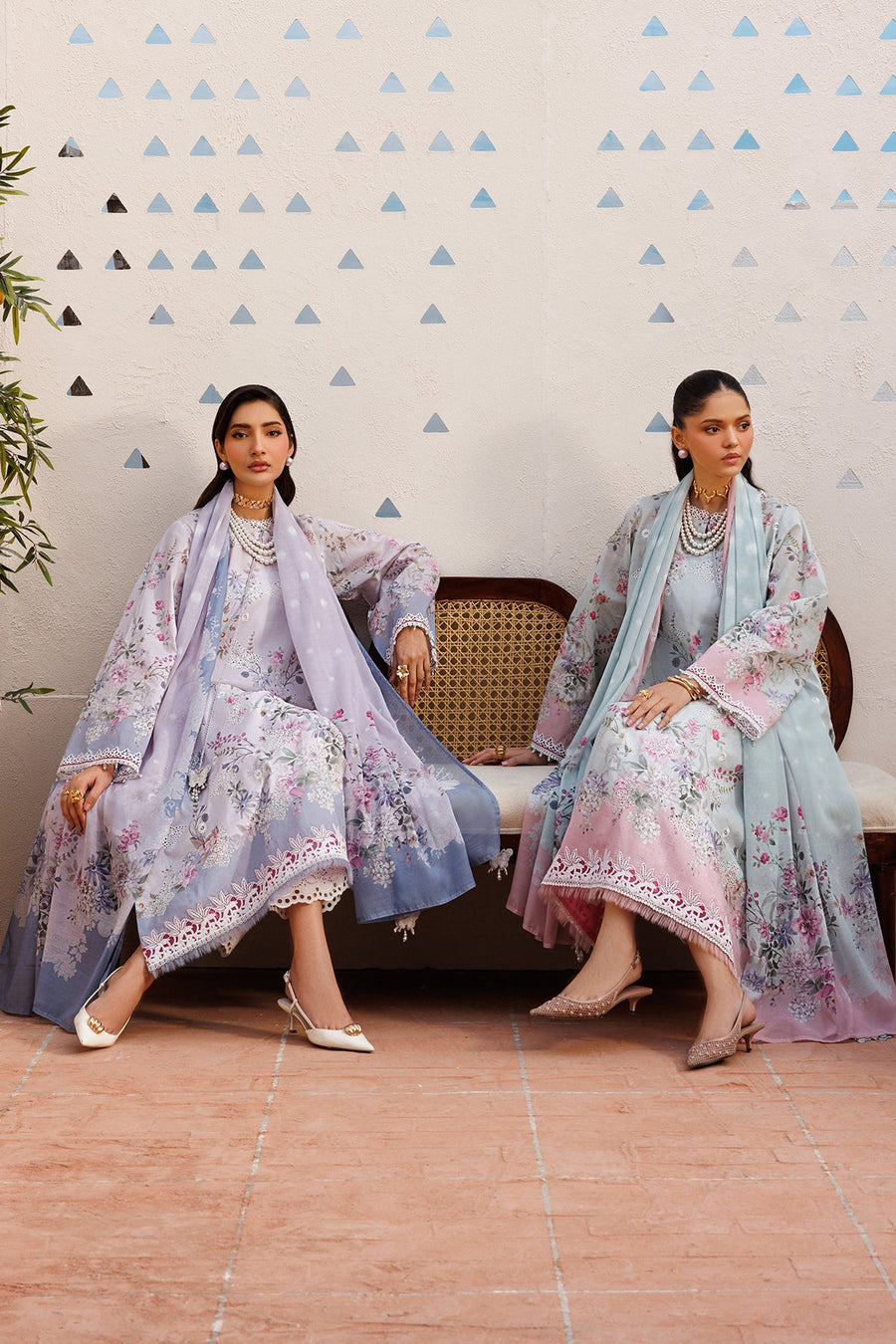 Full shot of two women wearing embroidered floral lawn suits, one in lavender and the other in a pastel blue-pink gradient, both accessorized with pearls and elegant shoes.
