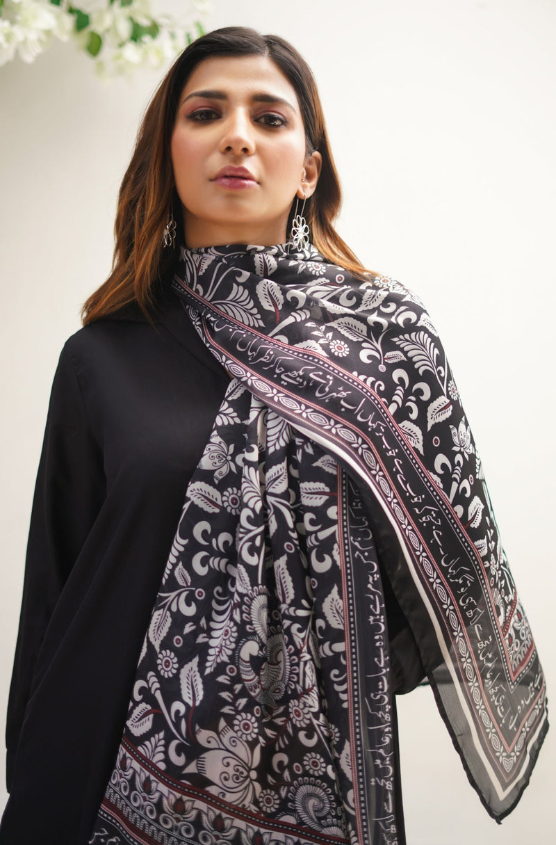 Woman wearing a black scarf with detailed white floral and calligraphy patterns draped elegantly over shoulder