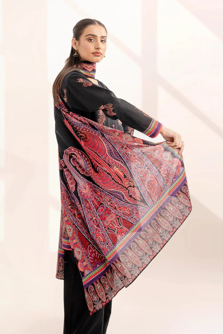 Side view of woman displaying the paisley printed dupatta in vibrant reds and purples against black outfit