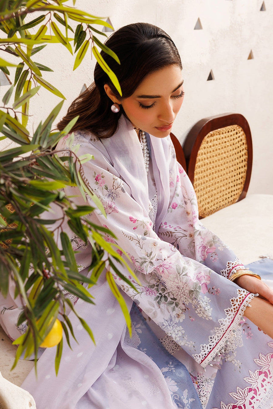 Model seated, displaying elegant pastel floral embroidered lawn suit with pearl necklace and white shoes.