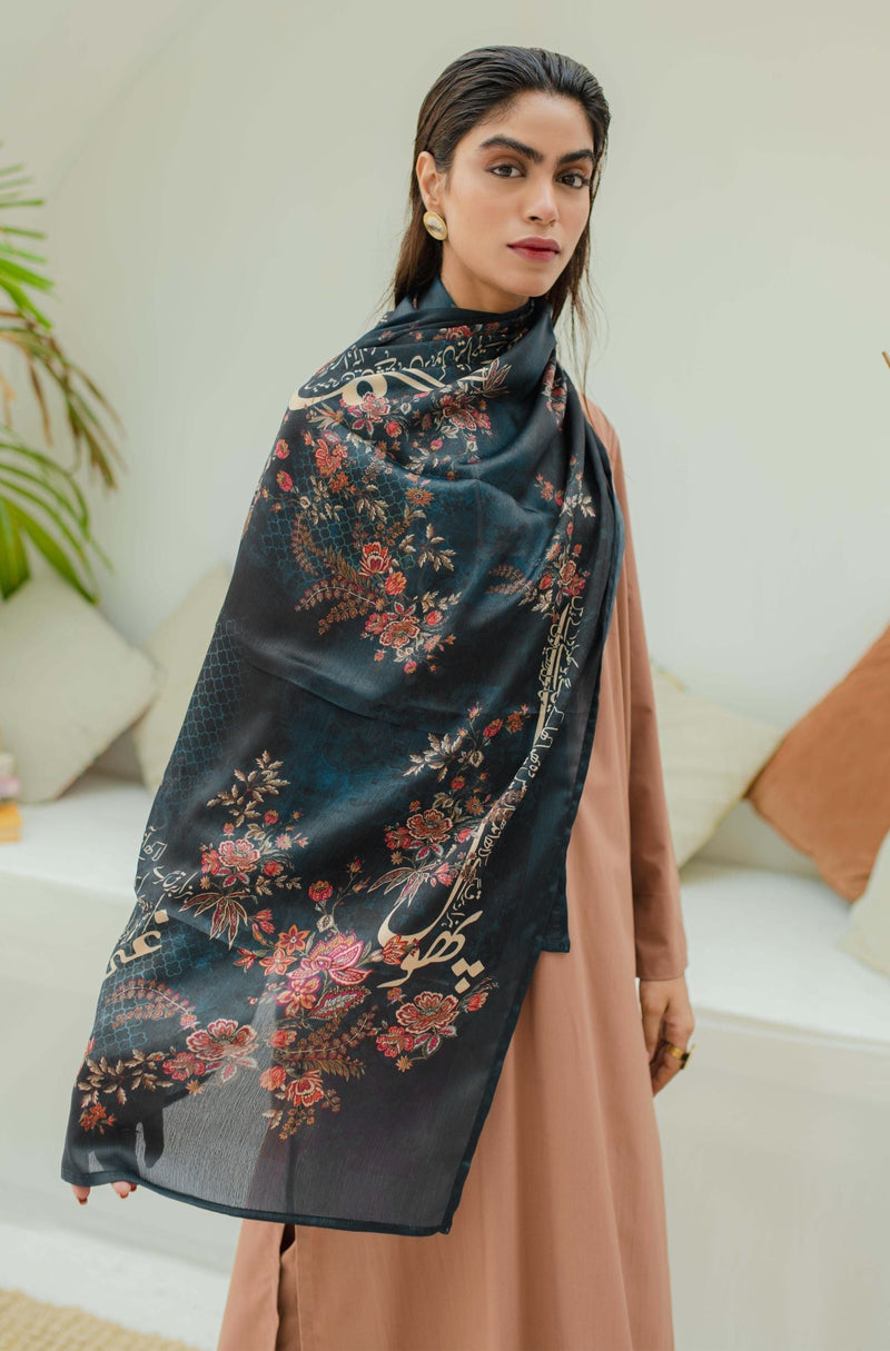 Woman wearing an elegant dark navy blue sheer scarf with intricate floral embroidery and Urdu calligraphy, paired with a peach dress and gold earrings